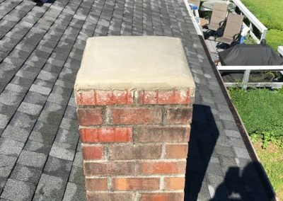 A brick chimney with a concrete cap on a shingled roof, overlooking a backyard with patio furniture.