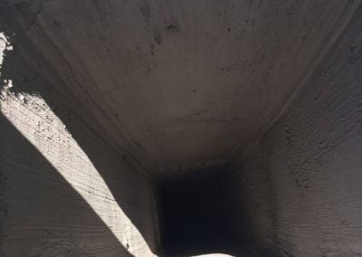 Inside view of an empty, rectangular concrete duct or tunnel with light at the entrance and darkness inside.