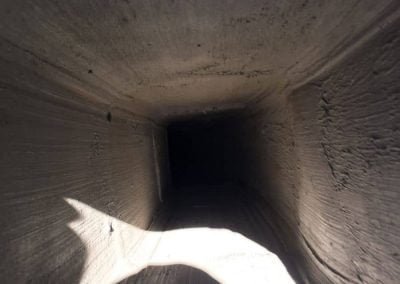 Inside view of a narrow, dusty ventilation duct or pipe with light shining on one side.