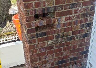 Brick wall with some missing bricks and a power tool on the ground. Tree and fence visible in the background.