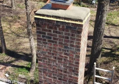 Aerial view of a brick chimney with a rooftop and backyard featuring trees, a patio set, and a ladder.