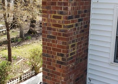 Brick chimney on a house next to a small patio with outdoor chairs and trees in the background.