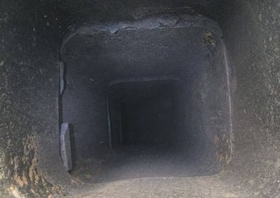 View looking down a dark, square chimney with rough, soot-stained interior walls.
