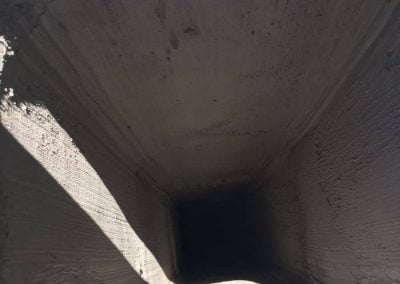 A view looking down a rectangular concrete tunnel or chute with light and shadow on the interior walls.