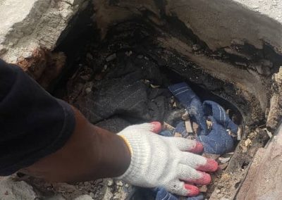 A gloved hand reaches into a hole in a concrete surface, touching fabric and debris inside.
