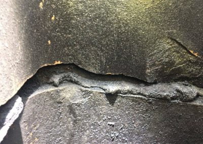 Close-up of a cracked, rough, and weathered dark surface with uneven texture and edges.
